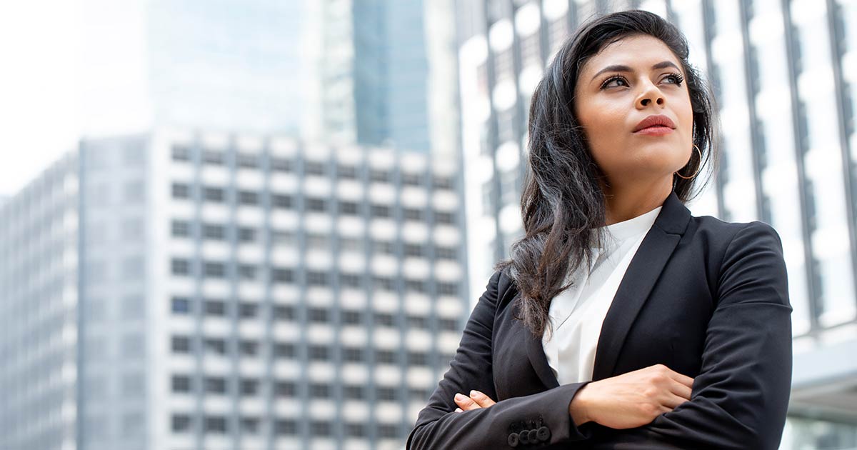 Businesswoman in a suit in the middle of a city looking up at different skyscrapers.
